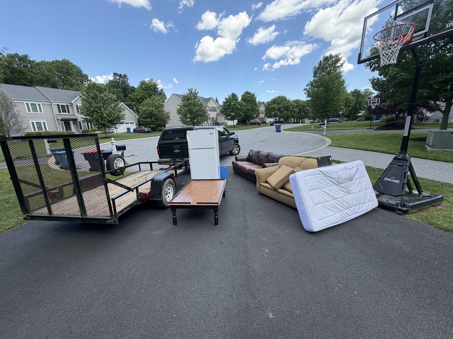 Fridge, couch, mattress and table staged in a driveway, ready for pickup